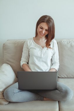 Bir dizüstü bilgisayar ile kanepede oturan genç kız