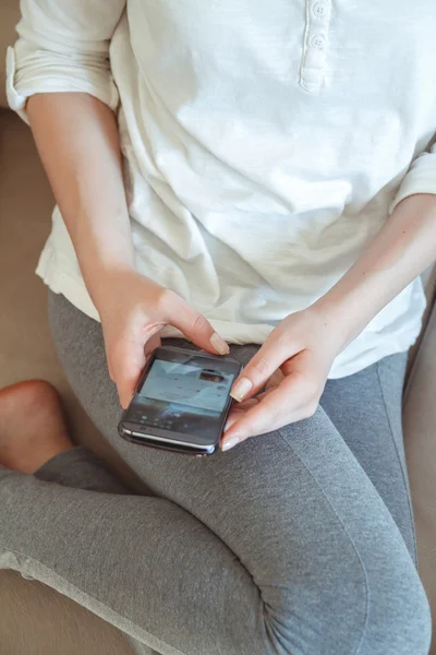 Chica en el sofá con el teléfono en la mano — Foto de Stock