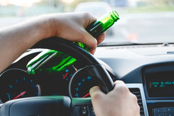 A man driving a car with a bottle of beer