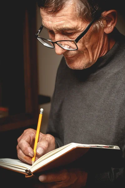 Пожилой человек, пишущий в блокноте — стоковое фото