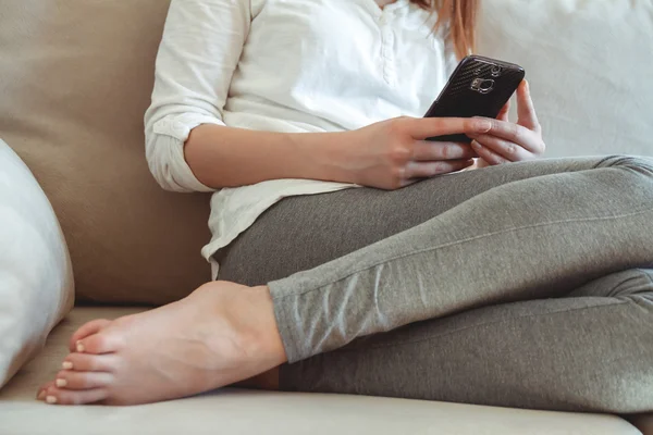 Chica en el sofá con el teléfono en la mano — Foto de Stock