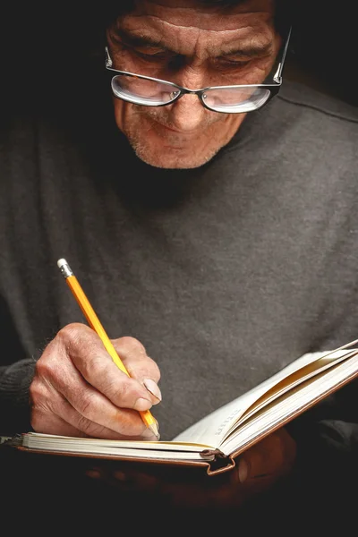 Un homme âgé écrit dans un cahier — Photo