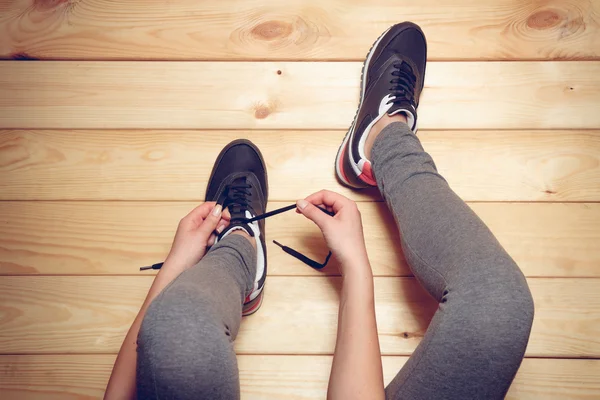 木製の床の上に座って靴紐を結ぶ少女 — ストック写真