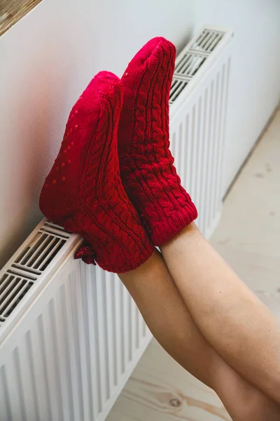 暖かい 居心地の良いニットの靴下の若い女性はラジエーターで彼女の足を暖めます — ストック写真