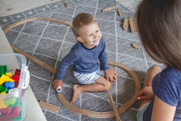 小男孩和他的母亲坐在地板上玩铁路 — 图库照片