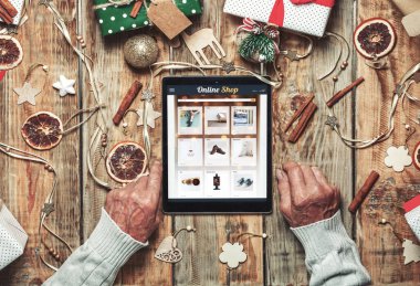 Elinde tabletle yaşlı bir adamın elleri Noel süslemeleri olan online alışveriş masasında.