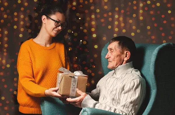 一位年迈的父亲和他年幼的女儿在一棵圣诞树的背景下送给并打开了一份圣诞礼物 — 图库照片
