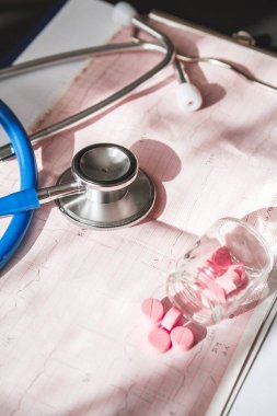 Hastanın tıbbi kartı, steteskop ve doktorun masasındaki haplar.
