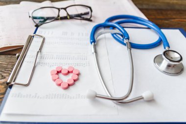 Hastanın tıbbi kartı, steteskop ve doktorun masasındaki haplar.