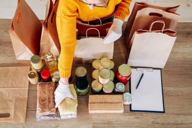 Tıbbi eldiven takan genç bir kadın, yiyecek bağışlarını kese kağıdına dolduruyor.