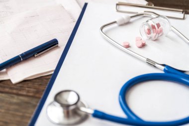Hastanın tıbbi kartı, steteskop ve doktorun masasındaki haplar.