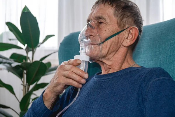 Yaşlı bir ihtiyar, evdeki karantinada oksijen maskesiyle bir koltukta oturuyor.