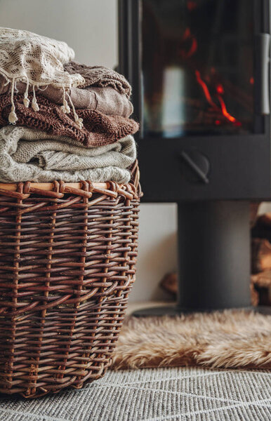A stack of warm clothes in a wicker basket an iron fireplace wit
