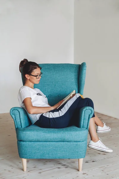 Νεαρή γυναίκα κάθεται στην πολυθρόνα και το βιβλίο ανάγνωσης, απομονωμένη — Φωτογραφία Αρχείου