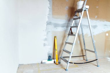 A stepladder with painting tools in a room in a house or apartment. Preparing for putty on the wall or painting. Home repair or renovation concept. clipart