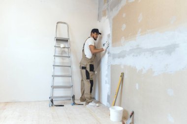 Elinde spatulası olan erkek ressam evde tamirat yapıyor. Oda yenileme konsepti.