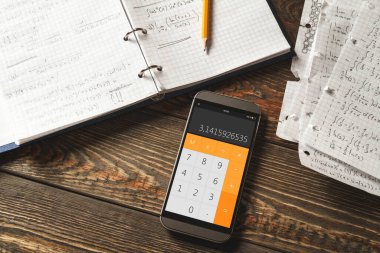 Matematiksel problemleri bir defterde çözmek. Ahşap masadaki hesap makinesi uygulamalı telefon..