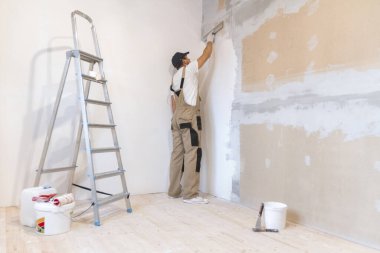 Male painter with a spatula in his hands makes repairs in home. Room renovation concept. clipart