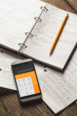 Matematiksel problemleri bir defterde çözmek. Ahşap masadaki hesap makinesi uygulamalı telefon..