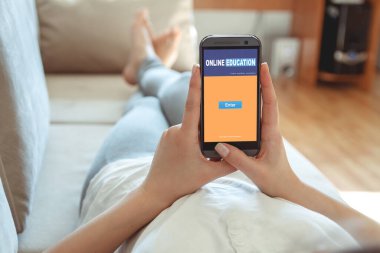 Kız elinde bir telefonla bir kanepede uzanıyor. Çevrimiçi eğitim kavramı.