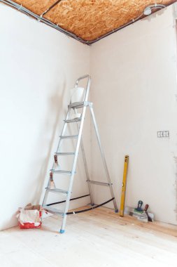 Evdeki ya da dairedeki bir odada boya aletleri olan bir merdiven. Duvardaki macuna ya da boyaya hazırlanıyorum. Ev onarımı veya yenileme konsepti.