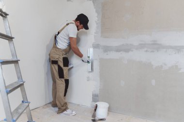 Elinde spatulası olan erkek ressam evde tamirat yapıyor. Oda yenileme konsepti.