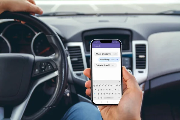 Young man driving a car with a phone in his hand. Multitasking. Don't text and drive