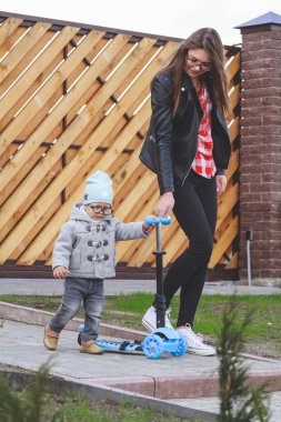 Çocuk ve anne dışarıda scooterlarla oynuyorlar. Çocuk için aktif eğlence ve açık hava sporu.