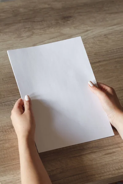 Mãos Femininas Com Uma Folha Papel Fundo Uma Mesa Madeira — Fotografia de Stock