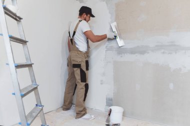 Elinde spatulası olan erkek ressam evde tamirat yapıyor. Oda yenileme konsepti.