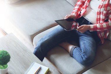 Kanepede oturan kadın tablet kullanıyor, el ele tutuşuyor.