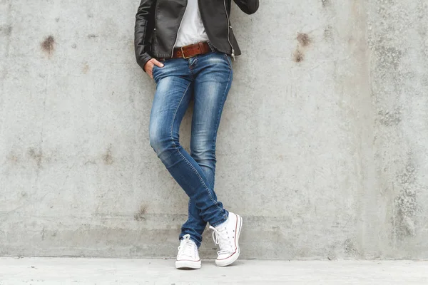 コンクリートの壁の近くのスニーカーやジーンズの形をした女性の足 — ストック写真