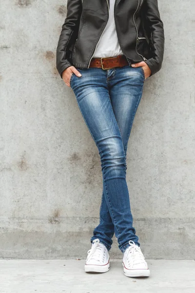 コンクリートの壁の近くのスニーカーやジーンズの形をした女性の足 — ストック写真