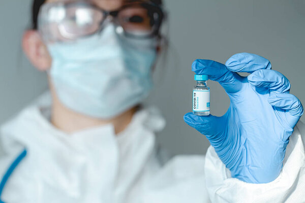 Врач или медсестра в защитном костюме, держащие в руках ковид 19 вакцины
