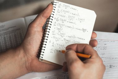 Matematik formülleri, elinde bir adam tutan bir defterde kurşun kalemle yazılır. Matematik problemleri.