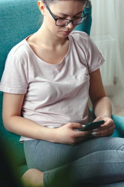 Genç bir kadın rahat bir koltukta otururken cep telefonu kullanıyor.