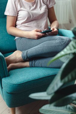 Genç bir kadın rahat bir koltukta otururken cep telefonu kullanıyor.
