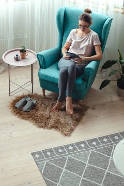 Rahat bir sandalyede otururken tablet kullanan genç bir kadın.