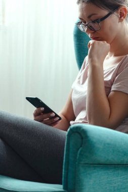 Genç bir kadın rahat bir koltukta otururken cep telefonu kullanıyor.