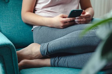 Genç bir kadın rahat bir koltukta otururken cep telefonu kullanıyor.