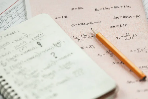 Math formulas are written in pencil on piece of paper, math problems