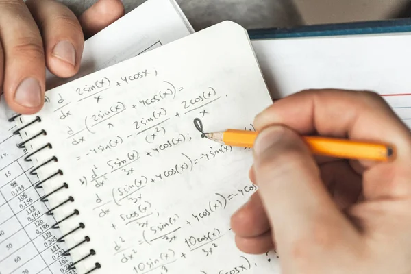 Math formulas are written in pencil in a notebook holding a man in hands, math problems