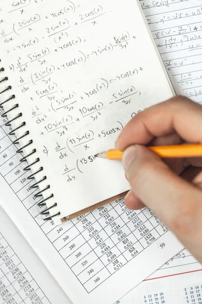 Math formulas are written in pencil in a notebook holding a man in hands, math problems