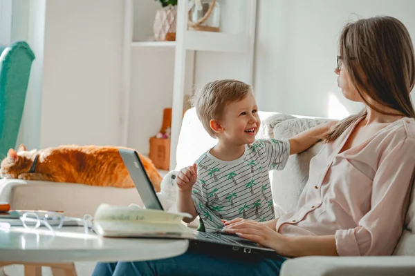 Concept of work at home and home family education, mother working with laptop at home, child playing nearby