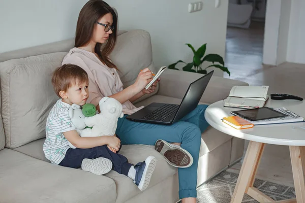 Concept of work at home and home family education, mother working with laptop at home, child playing nearby