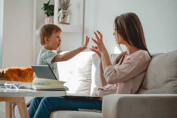 Concept of work at home and home family education, mother working with laptop at home, child playing nearby