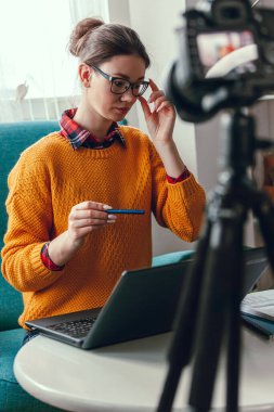 Kadın antrenör veya psikolog çevrimiçi konferans düzenliyor ve evdeki blog için kameraya video kaydediyor.