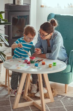 Mother or art therapist and child paint watercolor together at home