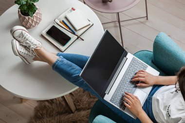 Genç bir kadın dizüstü bilgisayarını boş kullanıyor, modellik yapıyor, evde çalışıyor, üst katta çalışıyor.