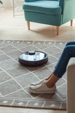Robot elektrikli süpürge temizlik halısı, kadın bacakları evdeki kanepede dinleniyor.